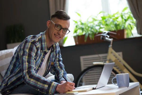 Concepto moderno de oficina independiente en casa. Joven inteligente en gafas de trabajo portátil en el interior del hogar. Ángulo holandés. Vista lateral — Foto de Stock