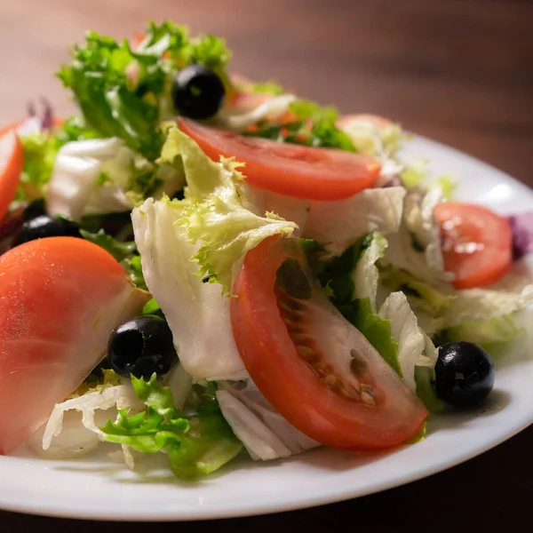 Kleurrijke natuurlijke vitamine voorgerecht. Verse groentesla met tomaten en olijven. Mooie lente lichte maaltijd of verfrissing op witte plaat. Gezond voedsel concept. close-up schot — Stockfoto