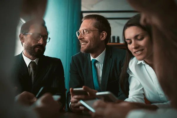 Grupo de empresários sorrindo usando telefones enquanto se comunica em reunião ou negociação. Conceito de parceria empresarial. Imagem matizada — Fotografia de Stock