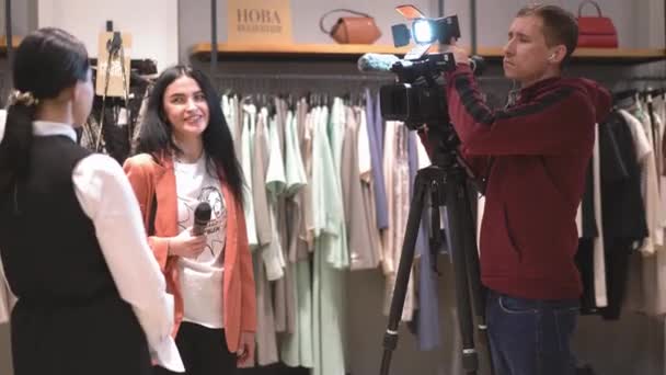 Un journaliste interroge une fille. Guy cameraman filme l'interview. Dans le fond du rack avec des vêtements. Images 4k de haute qualité. 27 mars 2019. Kiev, Ukraine — Video