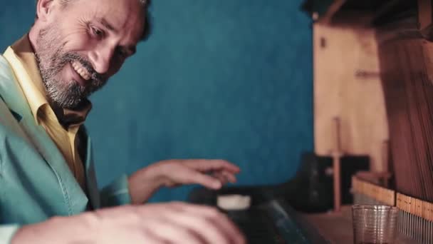 L'homme barbu joue du piano. Un homme d'âge moyen vêtu d'une veste finit de jouer de l'instrument et boit du whisky dans un verre. Il sourit à la caméra. Des images FullHD de haute qualité — Video