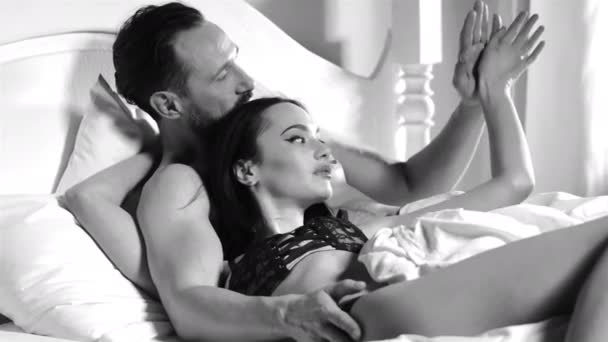 Муж и жена лежат утром в постели и обнимаются. Пара в нижнем белье. Черно-белая стрельба. Муж целует жену в затылок. Высококачественные 4k кадры — стоковое видео