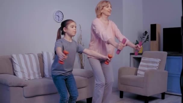 Old blond woman and young brown haired girl do sport. Healthy life conception. Workout at home. Grandma and granddaughter relationship — Stock Video