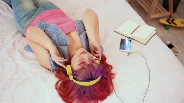 Νέοι συν μέγεθος κορίτσι με ροζ μαλλιά ακούστε μουσική στα ακουστικά στο κρεβάτι. Χαλαρωτικές και ανατριχιαστικές δονήσεις. Σύλληψη τρόπου ζωής. — Αρχείο Βίντεο