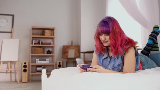 Jovem de cabelos cor-de-rosa está jogando jogos. Além disso, a rapariga do tamanho está a sorrir. Desfrutando de concepção de atividade em ambientes fechados. — Vídeo de Stock