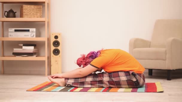 Een jonge vrouw met roze haar die thuis yoga doet. Thuis strekken — Stockvideo