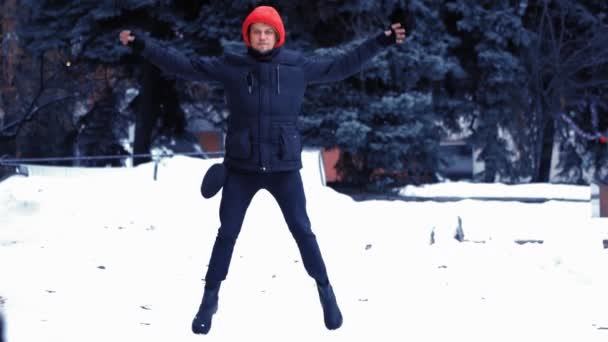 Parque de Inverno. Um homem de roupas pretas salta contra um fundo de abeto. A carregar ao ar livre. Conceito de aptidão inverno. — Vídeo de Stock