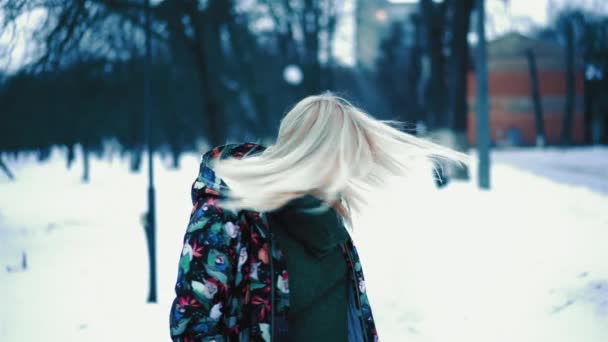 Covardes loiros com o cabelo em câmara lenta. Uma mulher de meia-idade em uma jaqueta colorida fica no fundo de um jardim de neve e sorri. — Vídeo de Stock