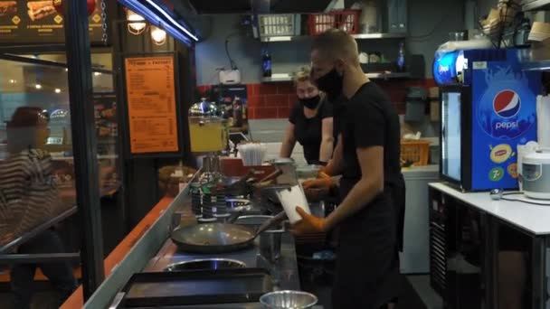 Dva kuchaři vaří jídlo pro zákazníka. Kuchaři nosí černou masku a oranžové rukavice, aby se ochránili. Zdravá, vyvážená, dieta, jídlo. Venkovní životní styl. 7. srpna2020. Kyjev, Ukrajina. — Stock video