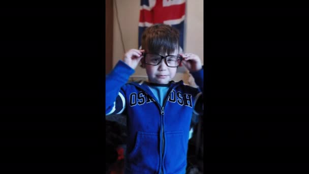 Leuk jongetje in blauw jasje met rits zet een grote bril op. Grappige momenten. Een glimlach. Mobiele video. 8 van juni 2020. Kiev, Oekraïne. — Stockvideo