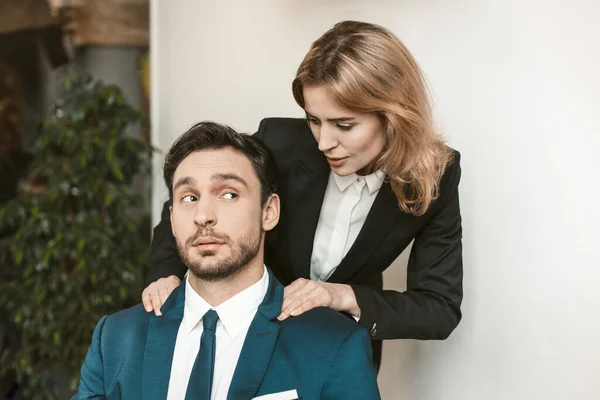 Patron féminin séduit employé. La jeune fille tient par les épaules un collègue assis à la table. Il la regarde avec surprise. Photo de haute qualité — Photo