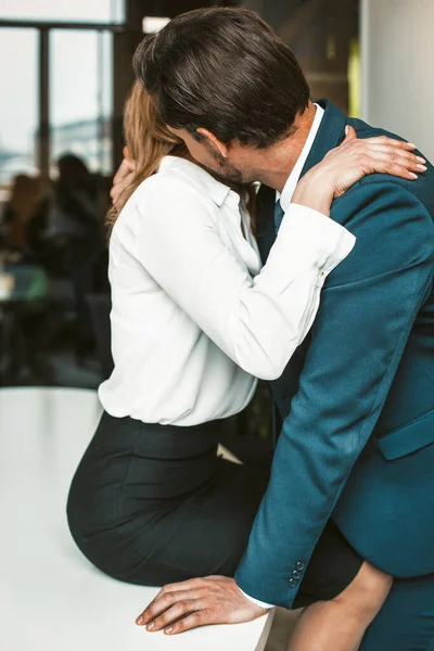 Egy irodai dolgozó ül az asztalon, miközben egy kolléga csókolgatja a nyakát. Szenvedélyes viszony az irodai munka koncepciójában. Kiváló minőségű fénykép — Stock Fotó