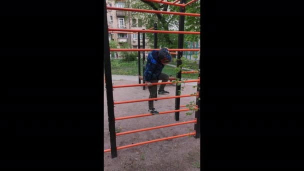 Mignon petit garçon en veste bleue jouer sur l'échelle des enfants orange. Des émotions joyeuses, amusantes et joyeuses. Jouer à la vidéo mobile de l'aire de jeux. 8 juin 2020. Kiev, Ukraine. — Video