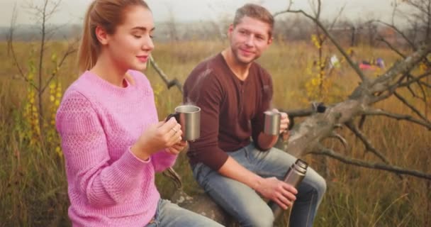 Jeune femme blonde assise à côté du jeune homme aux cheveux bruns. Couple boire une boisson chaude assis dans la forêt Marcher ensemble dans la forêt. Jolie conception de couple. Activités extérieures. Émotion de satisfaction — Video