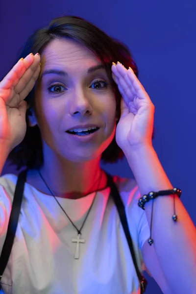 Jonge verraste vrouw gesloten met handen van licht op blauwe achtergrond. close-up schot — Stockfoto