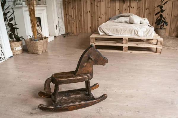 Bedroom in the interior of wood with a wooden horse. Theres a childrens horse in the foreground. In the background is a bed and a fireplace. High quality photo — Stock Photo, Image