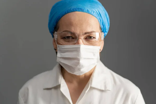 Femeie doctor fata, aproape împușcat. Femeia matură cu mască de protecție și ochelari de protecție se uită la cameră. Izolat pe gri — Fotografie, imagine de stoc