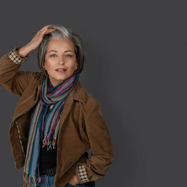 Sexy mid aged woman touches her graying hair and looks at the camera. Studio portrait of fashion lady in casual