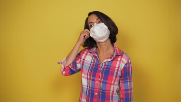 La joven se quita felizmente la máscara médica y la tira. Fondo amarillo en el estudio. Poner fin al concepto de cuarentena — Vídeos de Stock