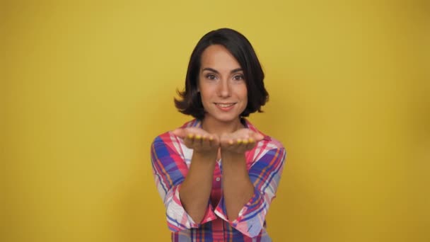 Junge brünette Frau streckte ihre Handflächen in die Kamera. Frau zwinkert dem gelben Hintergrund des Studios zu. — Stockvideo