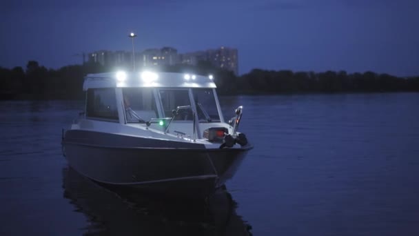 Båt med motorn på kvällen står på vattnet med lamporna tända. I bakgrunden skogen och byggnaderna. Hög kvalitet. 27 juli 2020. Kiev, Ukraina — Stockvideo