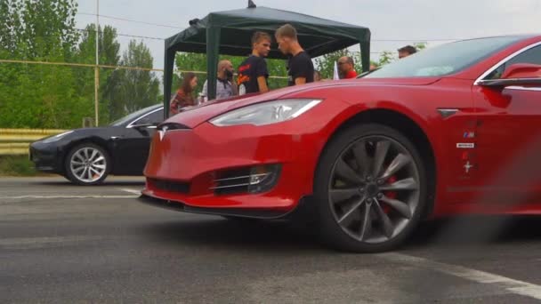 Yarışı başlatan iki Tesla arabası. Kırmızı ve siyah Tesla 'lar hızda yarışıyor. Aşağıdan yakın çekim. Ağır çekim. Arka planda, izleyiciler ve organizatörler. 24 Ağustos 2020. Kyiv, Ukrayna — Stok video