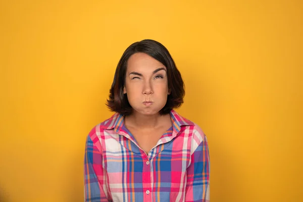 Young woman inflated her cheeks on a yellow background in the studio. She has bent her eyebrow and looks up. High quality photo — Stock Photo, Image