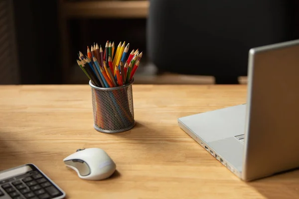 Oficina de trabajo. Lápices de color, ordenador portátil y ratón de la computadora en escritorio de madera en la oficina. Foto de alta calidad —  Fotos de Stock