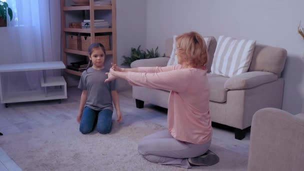 Grandmother and her granddaughter making physical jerks in the room. Indoors activities. Healthy lifestyle. Woman and child . — Stock Video
