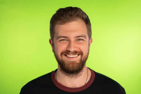 Кумедний бородатий чоловік широко посміхається на зеленому тлі. Портрет молодого щасливого чоловіка, який дивиться на камеру. Позитивна модель чоловічого кавказького фону на хромакі. Фотографія високої якості — стокове фото