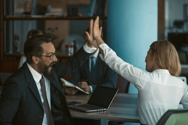 Man in a suit gives five to a woman in a blouse. Office workers work together. Theres a laptop on the table. Toned image. High quality photo