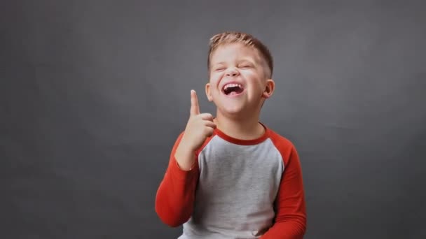 Verlichtende jongen lacht in de studio en laat zijn vinger zien. Jongen lacht op een geïsoleerde achtergrond. Hoge kwaliteit — Stockvideo