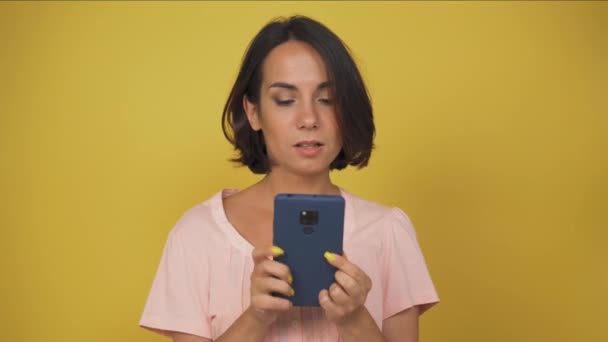 Una giovane donna tiene in mano un cellulare. Donna bruna spinge su smartphone su sfondo giallo. Alta qualità — Video Stock