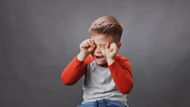 Menino chora no estúdio contra um fundo isolado. Rapaz soluça e limpa lágrimas com os punhos. Alta qualidade — Vídeo de Stock