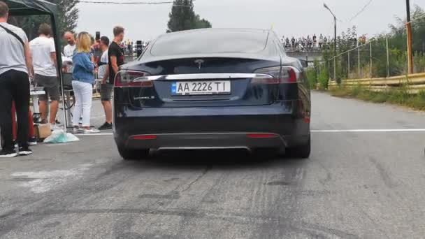 Teslas siyah elektrikli araba yarış dışı. Arkasından arabaya bak. Adam bir sonraki arabayı imzalıyor. Arka planda seyirciler var. Yüksek kalite. 24 Ağustos 2020. Kyiv, Ukrayna — Stok video