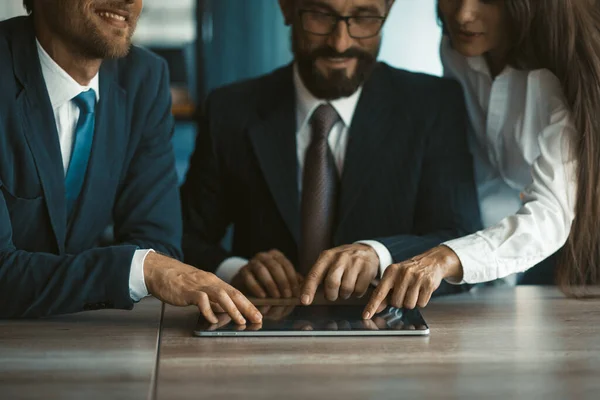 Colegas felizes usando o mesmo tablet digital juntos. Dois homens e uma mulher trabalham no escritório. Imagem cortada. Foco seletivo em mãos de empresários. Foto de alta qualidade — Fotografia de Stock