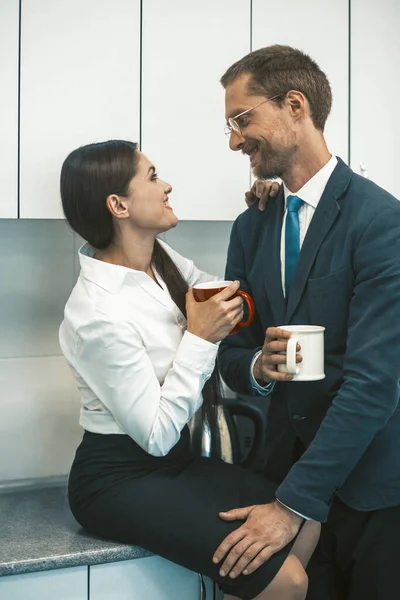Par dricker kaffe och flirtar under lunchen. Le man och kvinna hålla koppar varma drycker ser varandra. Kontorsromantik. Högkvalitativt foto — Stockfoto
