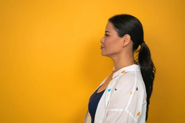 Femme d'âge moyen avec une peau parfaite regarde l'espace de copie. Vue du profil de jolie femme asiatique aux cheveux longs sur fond jaune — Photo