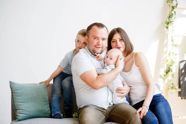 Photo of happy married couple with two young sons sitting on sofa — Stock Photo, Image