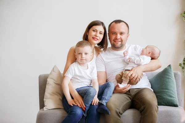 Imagen de padres sonrientes con dos hijos pequeños sentados en un sofá —  Fotos de Stock