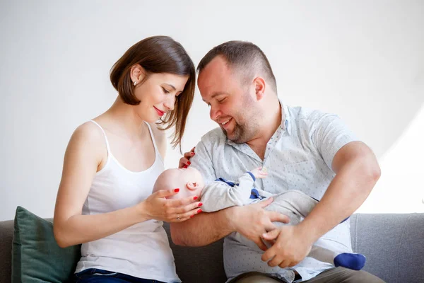 Retrato de padres jóvenes con bebé recién nacido sentado en el sofá —  Fotos de Stock