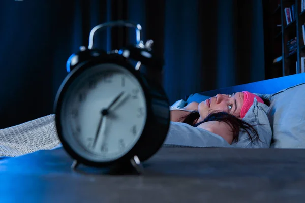 Foto di donna con insonnia con benda rosa occhio sdraiata sul letto accanto alla sveglia — Foto Stock