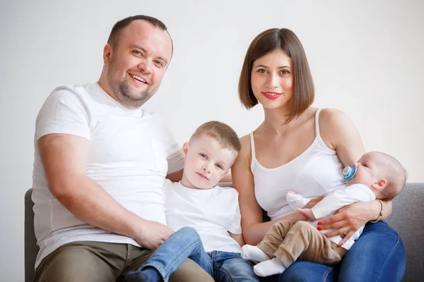 Imagem de casal feliz com dois filhos jovens sentados no sofá — Fotografia de Stock