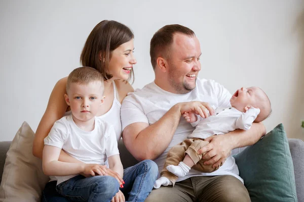 Imagem de mulher sorridente e homem com dois filhos jovens sentados no sofá — Fotografia de Stock