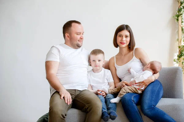 Foto de padres jóvenes felices con dos hijos pequeños sentados en el sofá —  Fotos de Stock