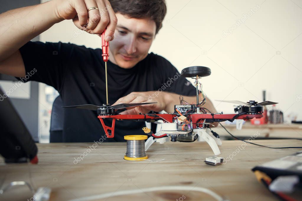 Photo of engineer with screwdriver fixing square copter at table
