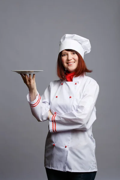 Foto de chef morena em roupão branco e boné com placa vazia na mão — Fotografia de Stock