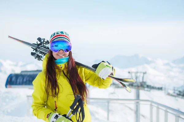 Mujer deportiva en máscara con esquís en el hombro en el fondo de la colina nevada, cielo azul en invierno — Foto de Stock