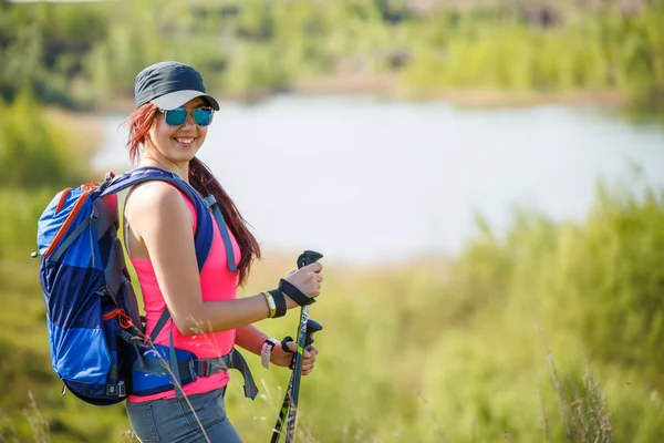 Foto di vista laterale di ragazza sportiva con bastoni da passeggio sullo sfondo del lago e vegetazione verde — Foto Stock