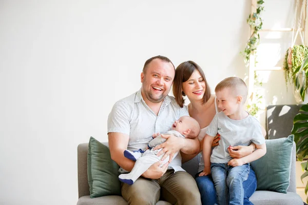 Foto de padres sonrientes con dos hijos pequeños sentados en el sofá —  Fotos de Stock